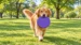 A golden retriever walking across a park lawn carrying the purple XL DuraToy Flying Disc in its mouth